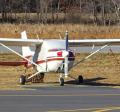 Red and white small aircraft parked at an airport with tie downs on the wing struts