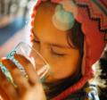 Selective focus photo of girl wearing a red tasseled cap drinking a glass of water