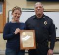 A woman and a man in a police uniform stand side by side. The woman is holding a plaque honoring the retiring police chief. 