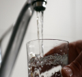 Close up of person's hand holding a glass under a running water faucet.