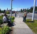 Photo of family sitting on bench and admiring a flower garden on the sidewalk at intersection of Pioneer Ave & Main St in Homer.
