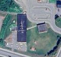 Aerial photo of a property with one large and one small building with a large parking lot on the north and a road to the south.