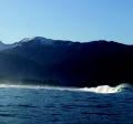 China Poot rip A large standing wave in an otherwise calm sea with mountains and a blue sky in the background.