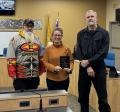 Three people standing next to each other in a City Council meeting room, two men and a woman in the middle holding an award.