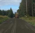 A freshly graded gravel road with a grader in the background.