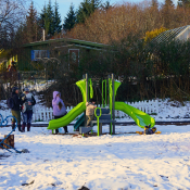 Two children in snowsuits playing on the slides of new lime green play structure.