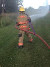 Back of Homer Volunteer Firefighter aiming fire hose at flames.