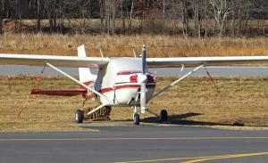 Red and white small aircraft parked at an airport with tie downs on the wing struts