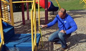 Man measuring the height of a playground component platform at a park in Wisconsin.