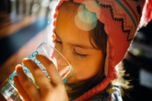 Selective focus photo of girl wearing a red tasseled cap drinking a glass of water