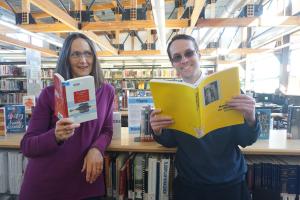 Retiring Library Director Ann Dixon holds up a book while looking at incoming Library Director Dave Berry who is also holding a 