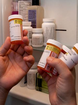 Two hands holding prescription drug containers in front of medicine cabinet.