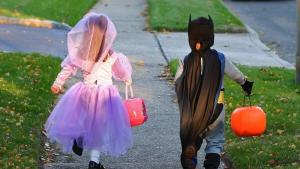 Trick-or-Treat Kids Two kids walking down sidewalk in Halloween costumes and holding treat bags shaped like jack-o-lanterns.