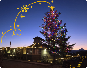 A large spruce tree lit with colored lights next to Homer City Hall with white lights against a dawn background 
