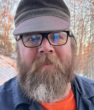 A bearded man with glasses and a wool hat