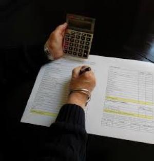 Woman's hand writing in a ledger with right hand and holding calculator ing the left hand