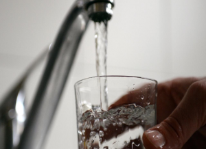 Close up of person's hand holding a glass under a running water faucet.