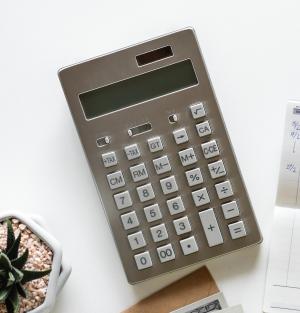 gray calculator on white table next to a small potted succulent plant