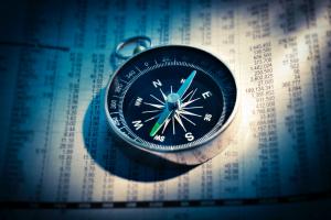 Close up photo of compass sitting on top of newspaper with columns of numbers