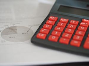 Black calculator with red keys sitting on white paper with a pie chart