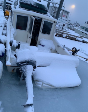 A snow-covered boat sitting low in the slushy harbor
