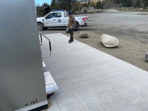 City staff person standing on concrete pad in front of a mobile restroom unit with a white pickup truck parked in the background