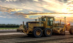 A large grader smoothing gravel at the Homer Airport with sunset colors in the sky.