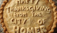 The top of a baked pie with fluted edges and dough lettering saying Happy Thanksgiving from the City of Homer