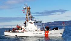 The USCG cutter Naushon on the waters of Kachemak Bay with blue sky and mountains in the background.