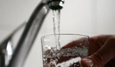 A hand holding and filling a drinking glass from a running kitchen faucet.