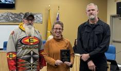 Three people standing next to each other in a City Council meeting room, two men and a woman in the middle holding an award.