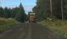 A freshly graded gravel road with a grader in the background.
