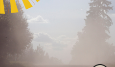 A photograph of a dusty tree-lined gravel road with graphics of a yellow sun and brown dust cloud overlain.